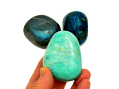 One big green amazonite tumbled crystal on hand with background with blue apatite and labradorite