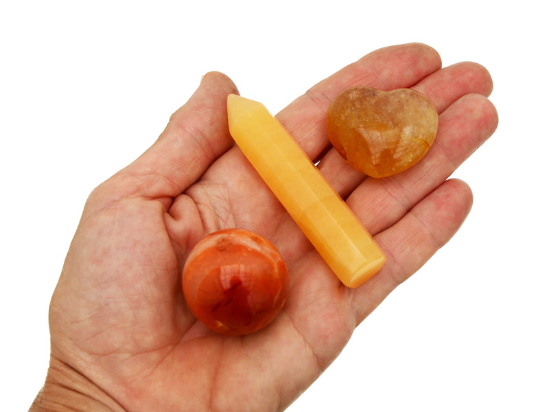 Small faceted orange calcite  crystal point, golden healer quartz heart and carnelian sphere on hand with white background