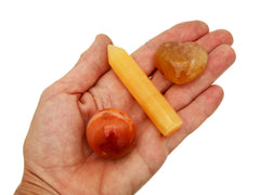 Small faceted orange calcite  crystal point, golden healer quartz heart and carnelian sphere on hand with white background
