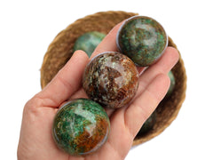 Two chrysocolla crystal spheres 45mm-50mm on hand with background with some crystals inside a straw basket on white