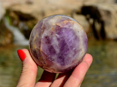 One amethyst crystal balls on hand with river landscape