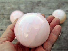 Natural pink mangano calcite sphere 55mm on hand with with some crystals on wood background