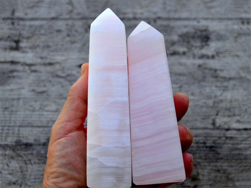 Two pink mangano calcite crystal obelisks 100mm-150mm on hand with wood background