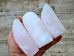 Three pink mangano calcite free forms 90mm-100mm on hand with wood background