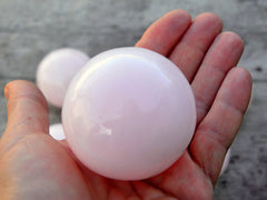 Pink mangano calcite sphere 50mm on hand with wood background 