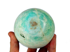 One large caribbean blue calcite sphere crystal 85mm on hand with white background