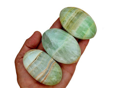 Three pistachio calcite palm stones 65mm-85mm on hand with white background