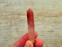 One mini rose calcite faceted point crystal 50mm on hand with wood background