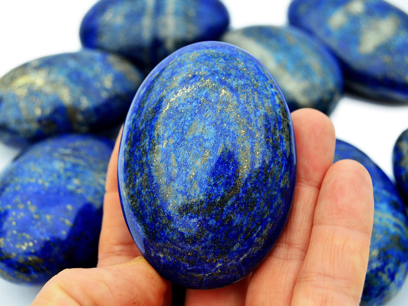 One lapis lazuli palm stone on hand with background with some crystals on white