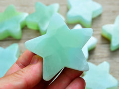 One green pistachio calcite star shapped crystal 60mm on hand with background with some stars on wood table