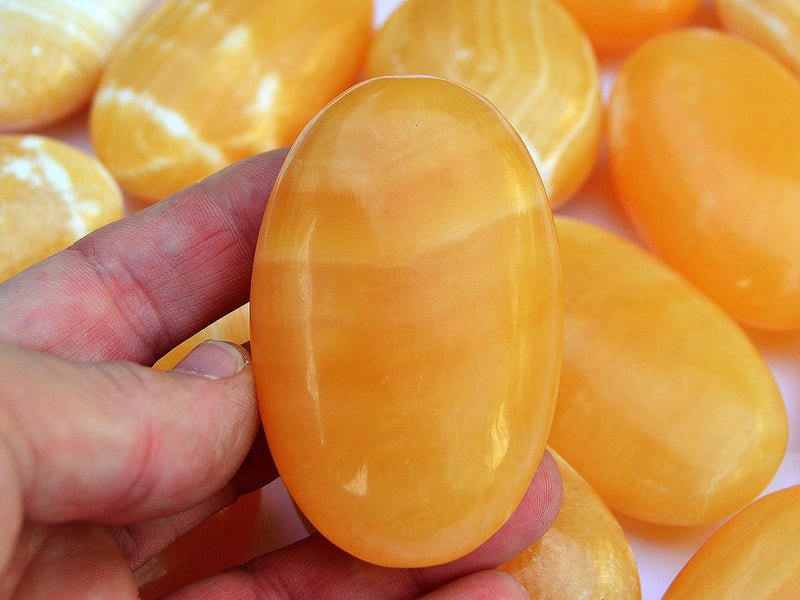 One orange calcite palm stone 60mm on hand with background with some crystals