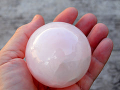 Pink mangano calcite sphere 55mm on hand with wood background 