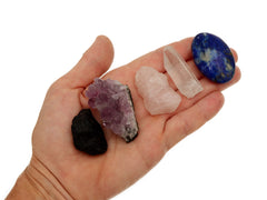 Raw black tourmaline, druzy amethyst, raw rose quartz, raw clear quartz point and lapis lazuli palm stone on hand with white background
