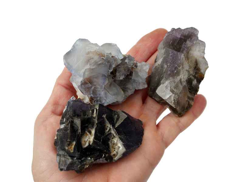 Three rough cubic purple fluorite crystals on hand with white background