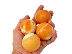 Four orange calcite mineral spheres 45mm on hand with white background