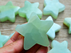 One green pistachio calcite star crystal 60mm on hand with background with some stars on wood table