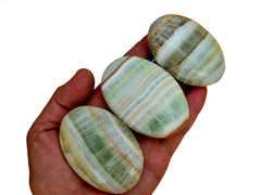 Three pistachio calcite palm stones 55mm-70mm on hand with white background