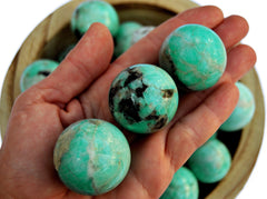 Three amazonite sphere crystals 25mm-40mm on hand with background with some crystals inside a wood bowl