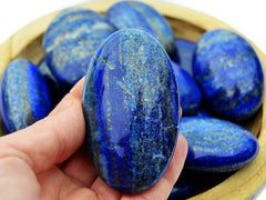 One lapis lazuli palm stone 70mm on hand with background with some stones inside a wood bowl