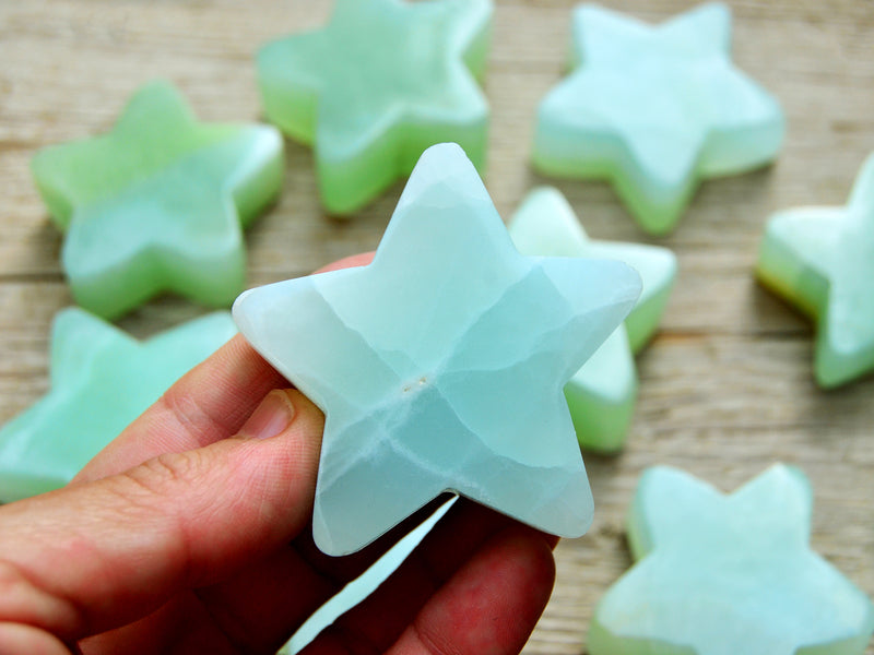 One green blue pistachio calcite star shapped mineral 60mm on hand with background with some stars on wood table