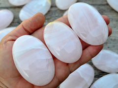 Three pink mangano calcite palm stone crystals on hand with background with some stones on wood table