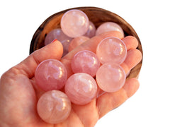 Several rose quartz crystal spheres 25mm - 40mm on hand with background with some balls inside a wood bowl