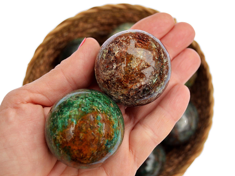 Two chrysocolla crystal spheres 50mm-50mm on hand with background with some crystals inside a straw basket on white
