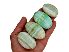 Four pistachio calcite palm stones 40mm-65mm on hand with white background