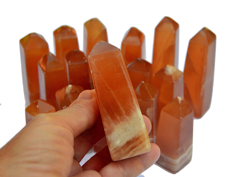 One natural honey calcite crystal obelisk 60mm on hand with background with several towers on white