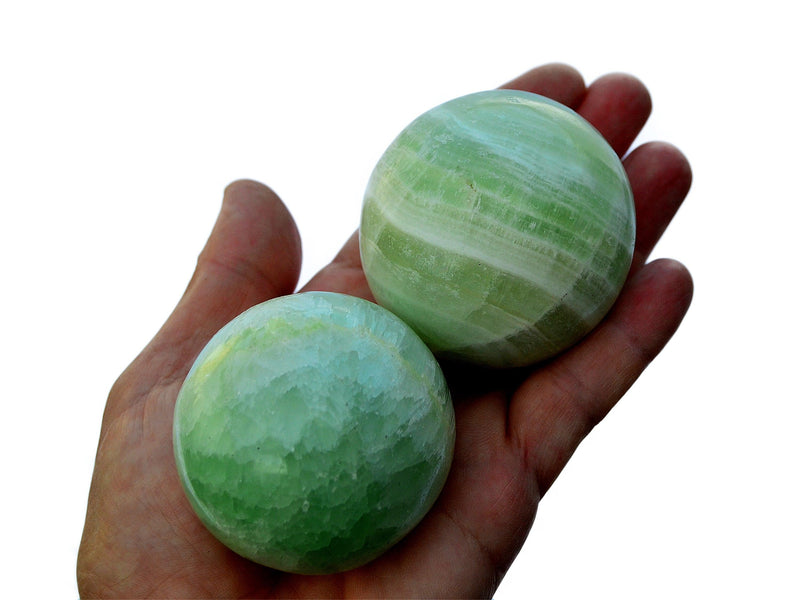 Two pistachio calcite spheres 50mm - 60mm on hand with white background