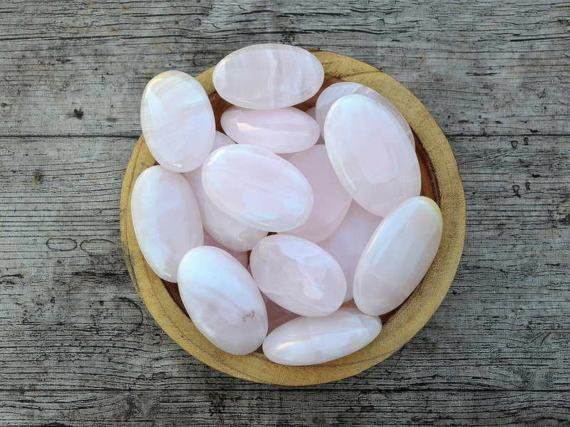 Several pink mangano calcite palm stones inside a wood bowl on wood table