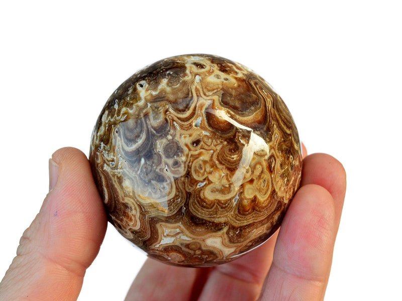 One brown chocolate and caramel calcite sphere crystal 55mm on hand with white background