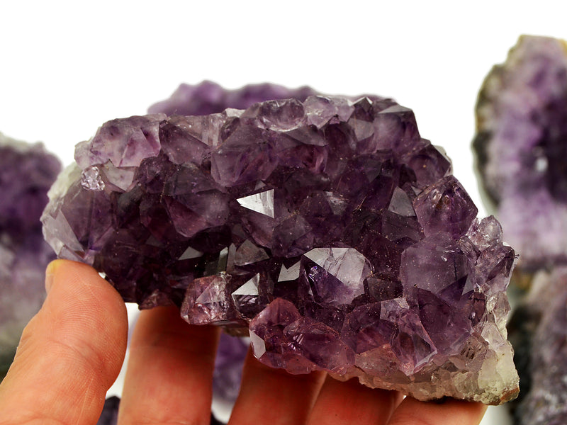 Raw druzy amethyst crystal held by a hand with a blurred background with some stones