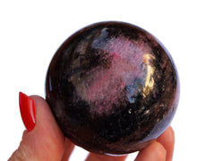 One pink and black rhodonite sphere mineral 55mm on hand with white background