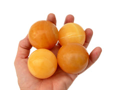 Four orange calcite sphere crystals 45mm on hand with white background