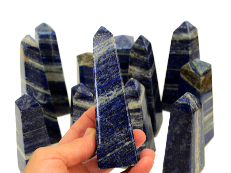 One lapis lazuli obelisk 120mm on hand with background with some lapis stones on white