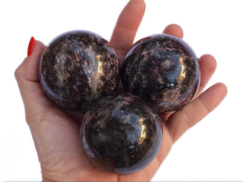 Four rhodonite crystal spheres 55mm-60mm on hand with white background