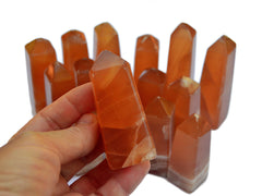 One honey calcite crystal tower 65mm on hand with background with several towers on white