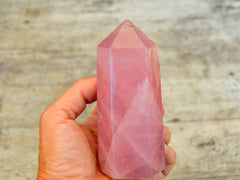 One chunky rose quartz tower crystal on hand with white background