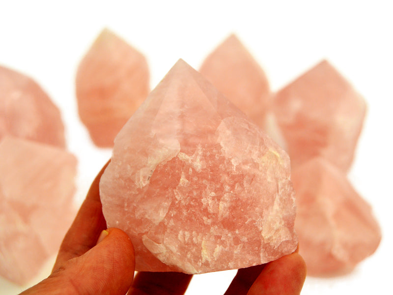 One pink quartz semi polished point 70mm on hand with background with some point stones on white