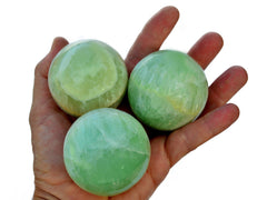 Three pistachio calcite spheres 40mm - 60mm on hand with white background