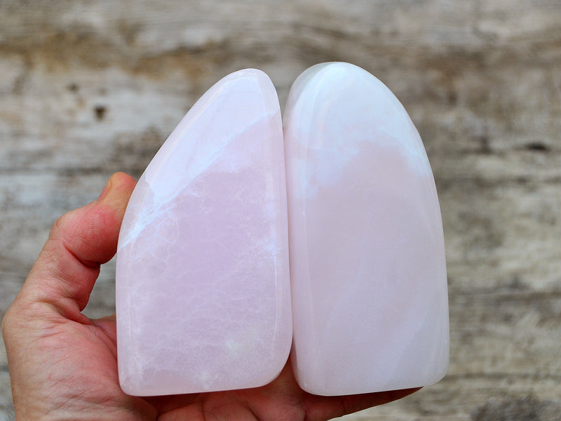 Two large pink mangano calcite free forms 100mm on hand with wood background