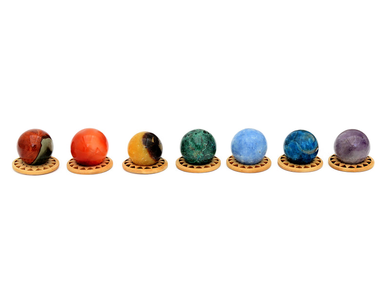 Mini spheres of polychrome jasper, carnelian, yellow septaria, chrysocolla, blue calcite, blue apatite and amethyst stones forming a horizontal line on wooden bases on a white background.