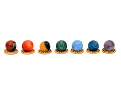 Mini spheres of polychrome jasper, carnelian, yellow septaria, chrysocolla, blue calcite, blue apatite and amethyst stones forming a horizontal line on wooden bases on a white background.