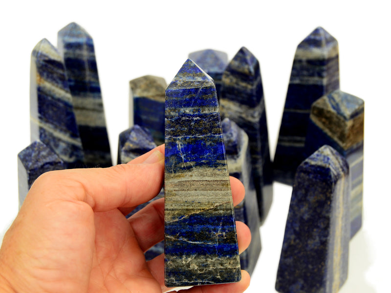 One lapislazuli obelisk 95mm on hand with background with some stones on white