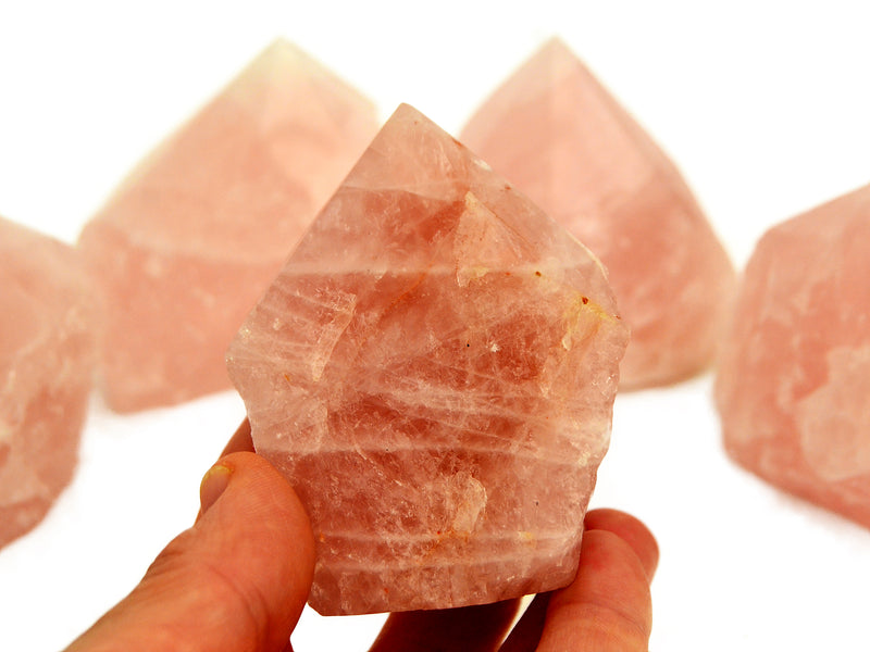 One pink quartz semi polished point 80mm on hand with background with some crystal points on white