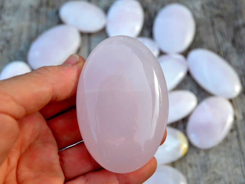 One pink mangano calcite palm stone 60mm on hand with background with some stones on wood table