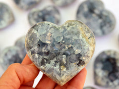 One big celestite raw heart on hand with background with some stone hearts on white