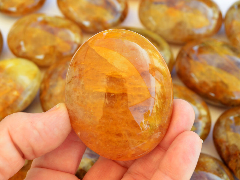 One golden healer quartz palm stone 65mm on hand with background with several crystals on white