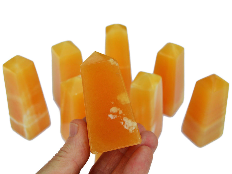 One orange calcite tower 60mm on hand with background with some obelisks on white background